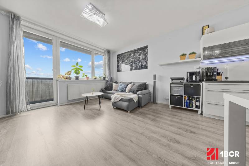 Obývací část 2-pokojového bytu s pohovkou, stolkem a podlahou s dřevěným dekorem.