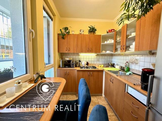 Kuchyně v jednopokojovém bytě s dřevěnými skříňkami a jídelním stolem.