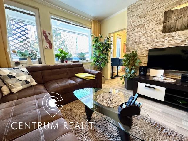 Obývací pokoj v 1-pokojovém bytě s hnědou sedačkou a podlahou s dřevěným dekorem.