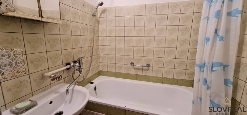 Koupelna se zrcadlem a vanou ve 3-pokojovém bytě, obložená dekorativními dlaždicemi.