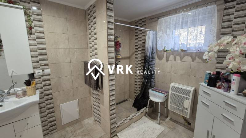 Koupelna v rodinném domě s obkladem a sprchovým koutem, dekorovaná květinami.