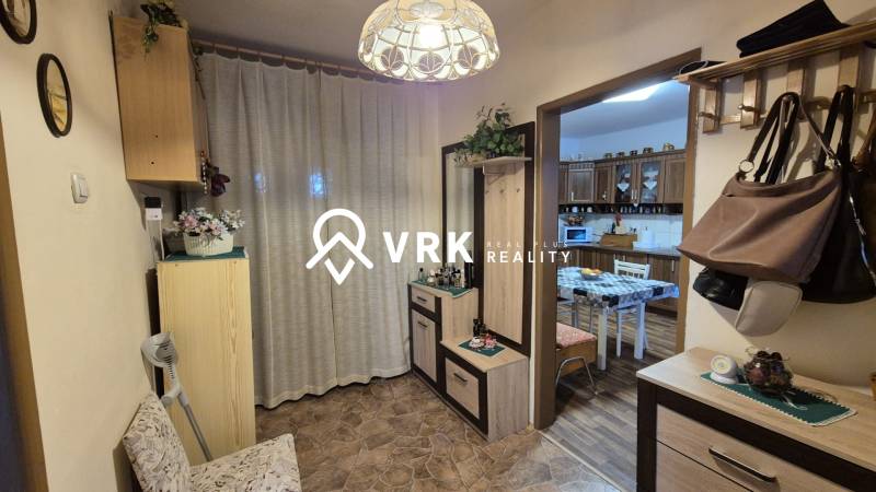 Předsíň v rodinném domě s věšákem, zrcadlem a vstupem do kuchyně s jídelním stolem.