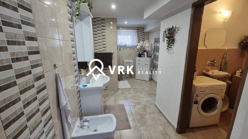 Koupelna v rodinném domě s kachličkovou stěnou, bidetem, pračkou a dekoracemi.