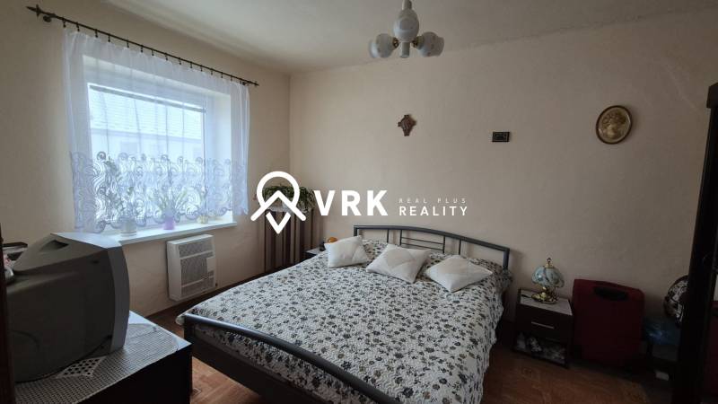 Ložnice v rodinném domě se vzorovaným přehozem, televizí a podlahou s dřevěným dekorem.