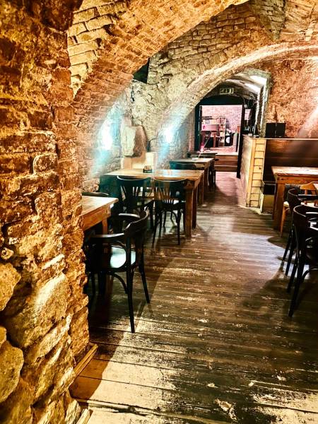 Kamenné oblouky, dřevěné stoly a podlaha s dřevěným dekorem v gastro prostorech.