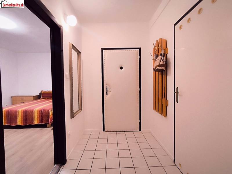 Chodba v 2-pokojovém bytě s bílými stěnami, dlažbou a zrcadlem.