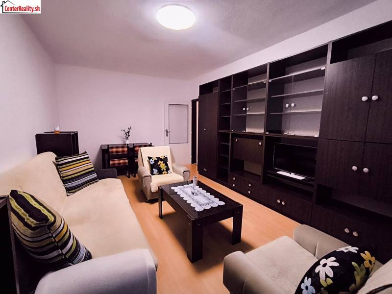 Obývací pokoj s pohovkou, křeslem, tmavým nábytkem a podlahou s dřevěným dekorem v 2pokojovém bytě.