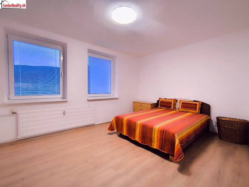 Ložnice v 2-pokojovém bytě s manželskou postelí, podlahou s dřevěným dekorem a jednoduchým nábytkem.