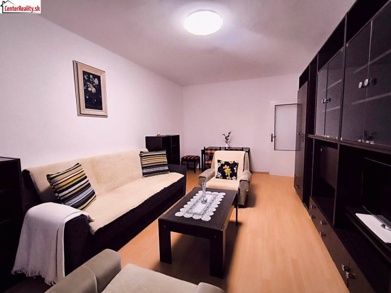 Obývací pokoj s pohovkou, dekorativními polštáři a podlahou s dřevěným dekorem ve 2pokojovém bytě.