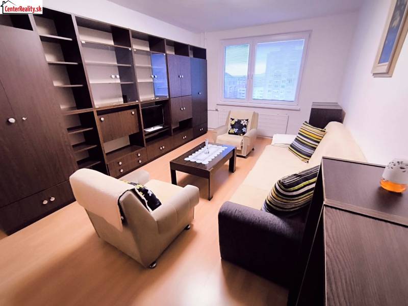 Obývací pokoj ve 2-pokojovém bytě s pohovkou, křesly a nábytkovou sestavou.