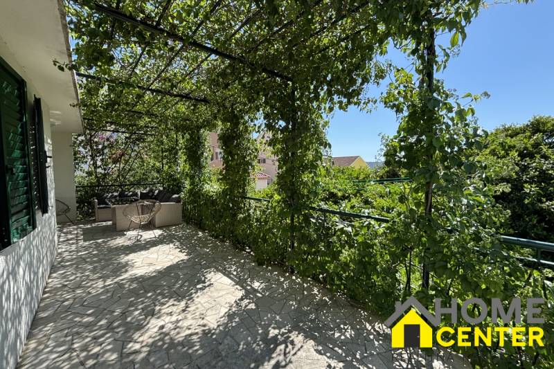 Terasa rodinného domu v Čiově s pergolou porostlou zelení a venkovním posezením.