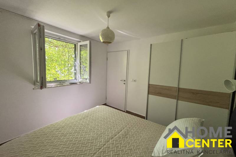 Světlá ložnice s oknem, bílou stěnou a skříní v rodinném domě.