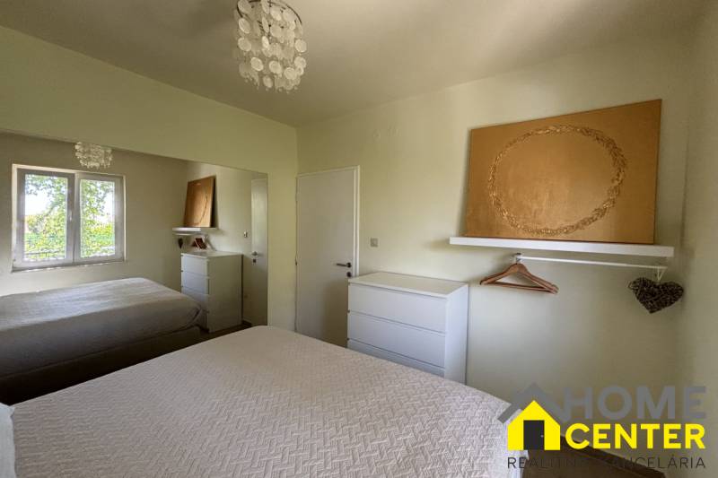 Ložnice v rodinném domě s bílým nábytkem, zrcadlem a texturovanými přehozy na postel.