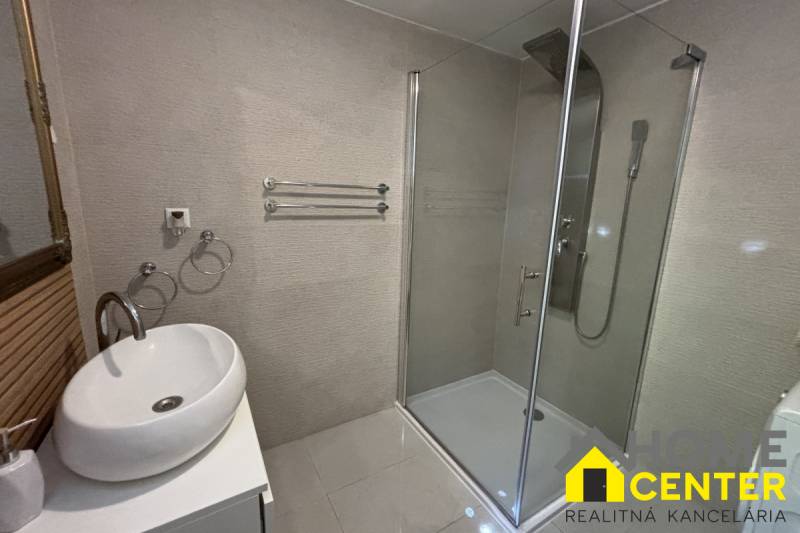 Koupelna v rodinném domě s umyvadlem, sprchovým koutem a držáky na ručníky.