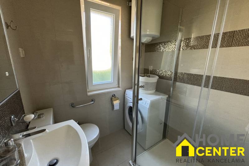 Koupelna v rodinném domě se sprchovým koutem, pračkou a oknem.