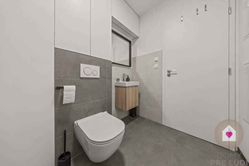 Koupelna s toaletou a umyvadlem ve 4-pokojovém bytě, šedé obklady, praktické úložné prostory.