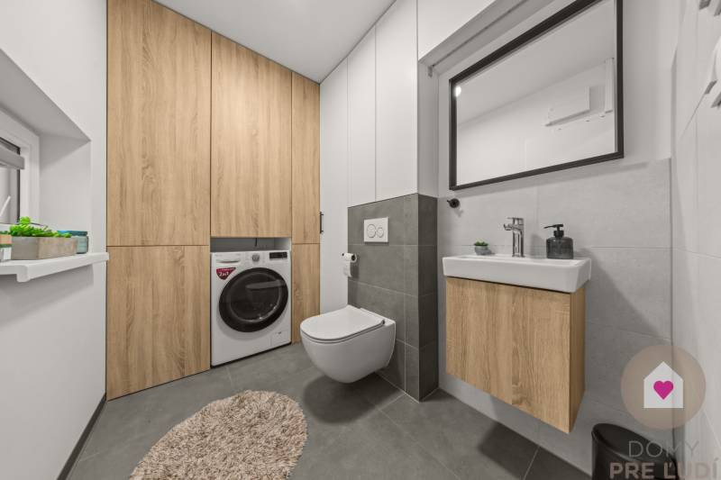 Koupelna se závěsnou toaletou, umyvadlem a pračkou se skříněmi ve 4-pokojovém bytě.