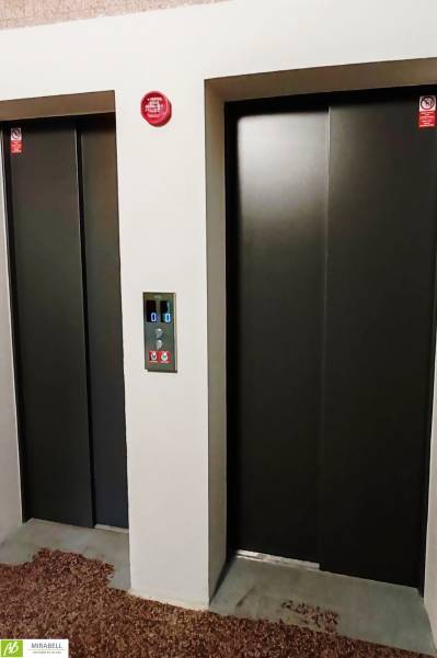 Dva výtahy s kovovými dveřmi a ovládacím panelem mezi nimi.