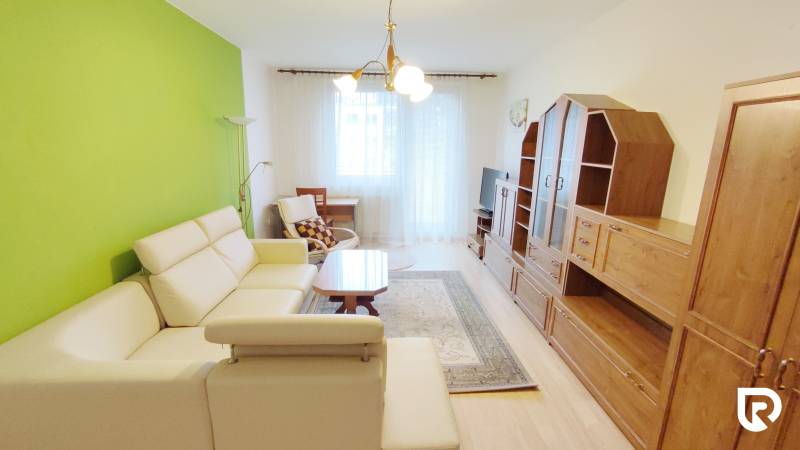 Obývací pokoj v 2-pokojovém bytě s krémovou sedačkou, zelenou stěnou a sestavou.