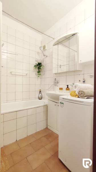 Koupelna v 2-pokojovém bytě se sprchou, umyvadlem a pračkou, světlé obklady.