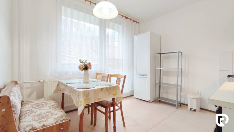 Kuchyně v 2-pokojovém bytě s jídelním stolem, židlemi a lednicí.