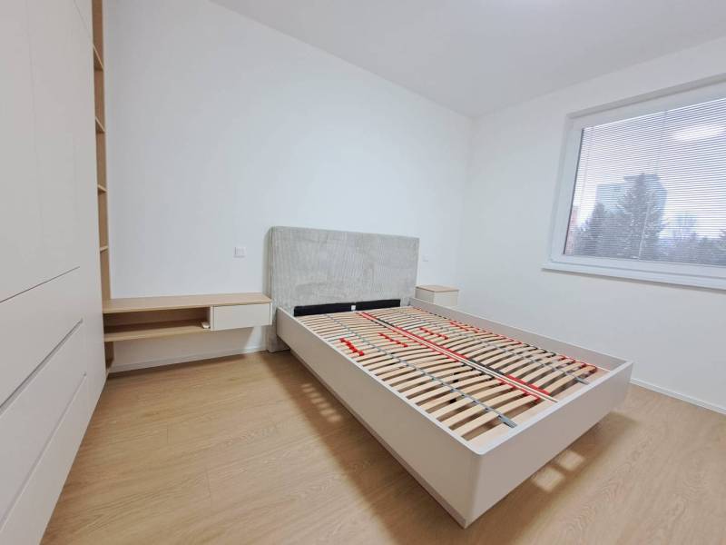 Ložnice v 2-pokojovém bytě s podlahou s dřevěným dekorem, velké okno, postel a úložný prostor.