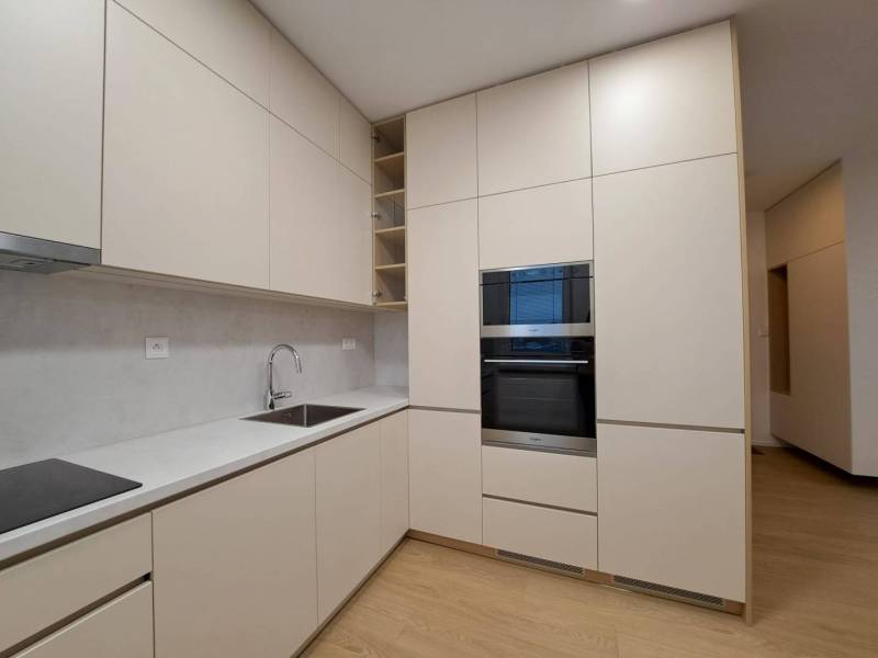 Kuchyně v 2-pokojovém bytě s podlahou s dřevěným dekorem, světlými skříňkami a vestavnou troubou.