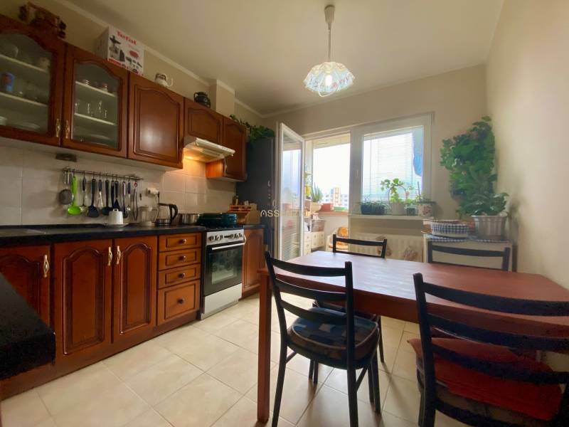 Kuchyně v 3-pokojovém bytě s dřevěnými skříňkami, jídelním stolem a oknem na balkon.