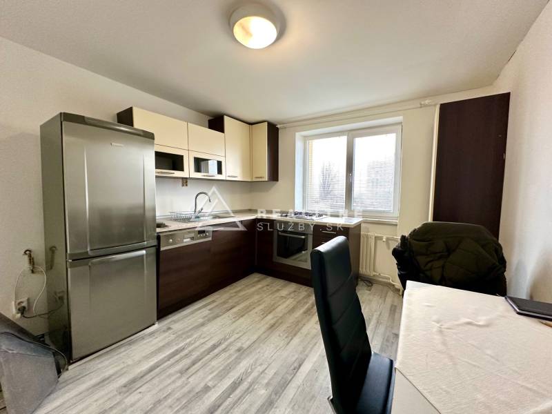 Kuchyně v 2pokojovém bytě s podlahou s dřevěným dekorem a stolem se židlemi.