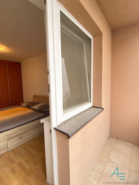 Ložnice v 2pokojovém bytě s postelí, podlahou s dřevěným dekorem a přístupem na terasu.