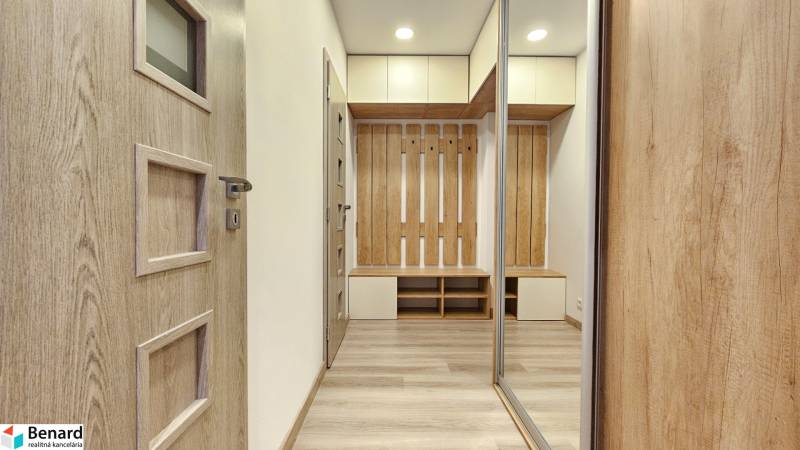 Interiér 1-pokojového bytu s podlahou s dřevěným dekorem, skříněmi a věšákovou stěnou.