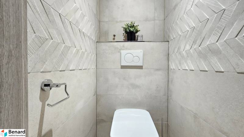 Koupelna v 1-pokojovém bytě s moderními obklady a dekorativní rostlinou.