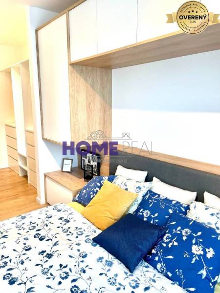 Ložnice v třípokojovém bytě s postelí, barevnými polštáři a úložnými prostory.