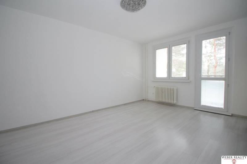 Pokoj v 3-pokojovém bytě s podlahou s dřevěným dekorem a velkými okny.