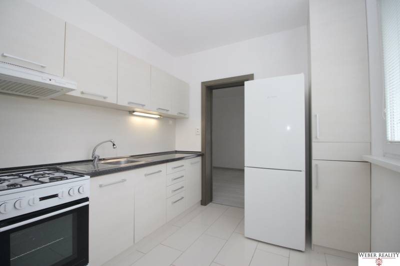 Kuchyně v 3-pokojovém bytě s bílými skříňkami a bílou podlahou.