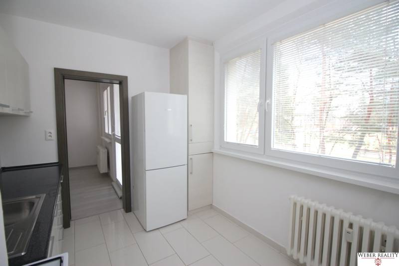 Kuchyně v 3-pokojovém bytě s velkými okny, lednicí a světlou dlažbou.