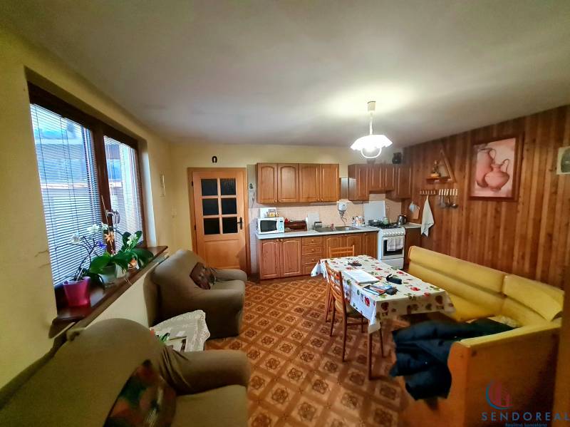 Kuchyně v rodinném domě s dřevěným dekorem, sedací soupravou a jídelním stolem.