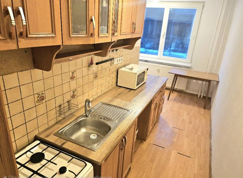 Kuchyně s podlahou s dřevěným dekorem a oknem, součást 3pokojového bytu.