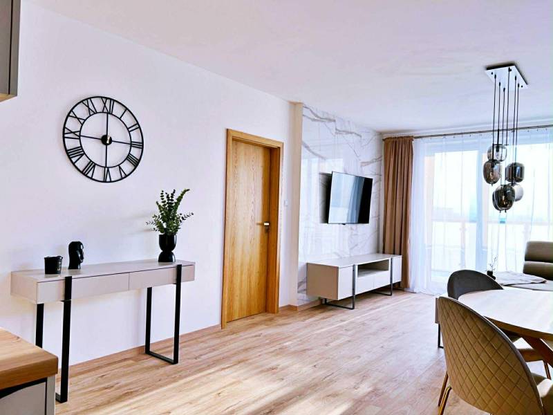 Obývací pokoj ve 3pokojovém bytě s podlahou s dřevěným dekorem, stolem a televizí.