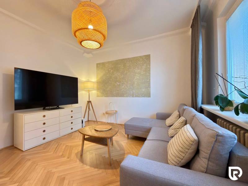 Obývací pokoj v 2-pokojovém bytě s podlahou s dřevěným dekorem, sedačkou a TV.