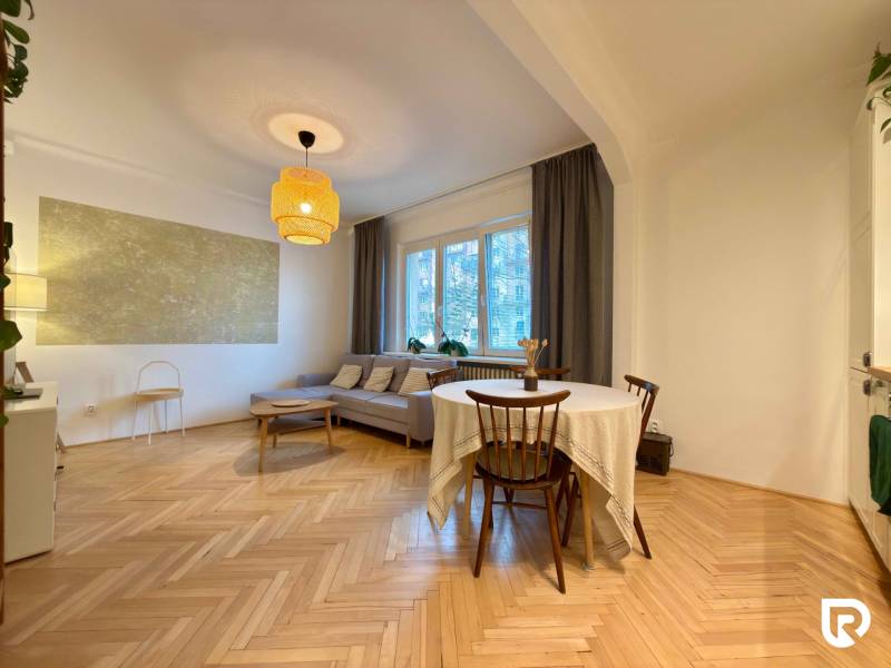 Obývací pokoj v 2pokojovém bytě s hnědou sedačkou a podlahou s dřevěným dekorem.