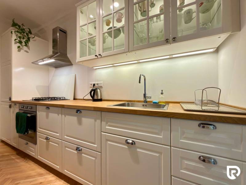 Světlá kuchyně v 2-pokojovém bytě s podlahou s dřevěným dekorem a bílými skříňkami.