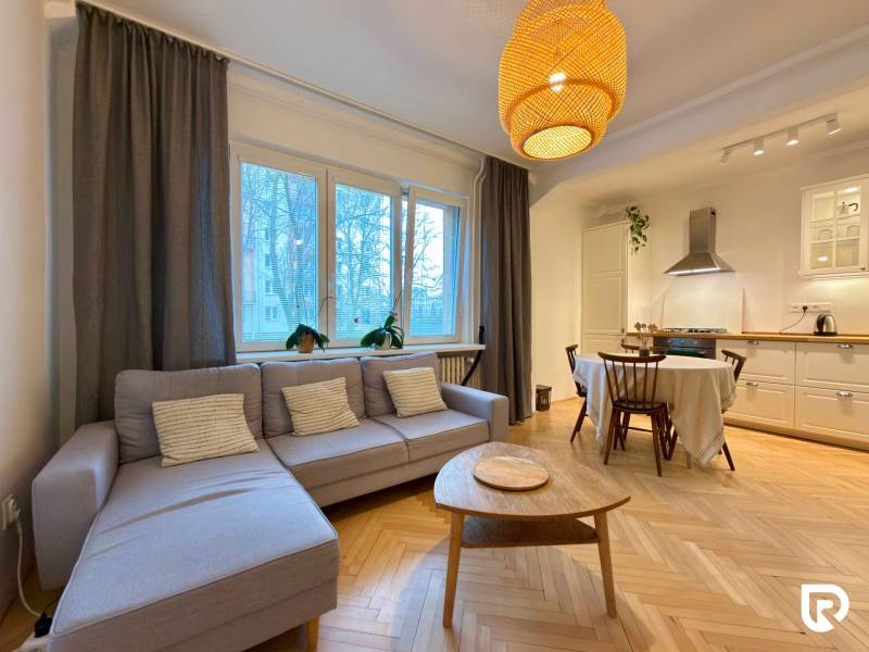 Obývací pokoj s kuchyní a jídelním stolem, podlaha s dřevěným dekorem, světlá sedačka.