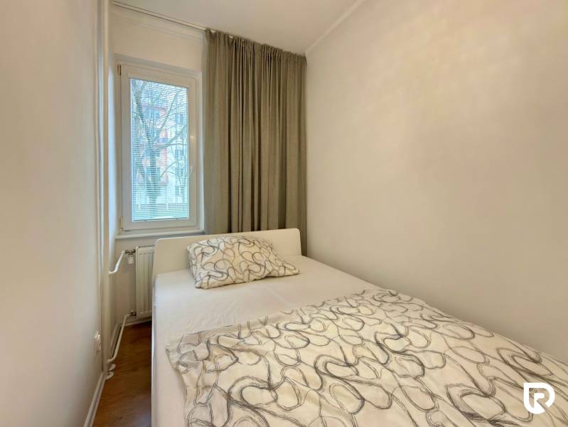 Ložnice v 2-pokojovém bytě s postelí, oknem a závěsy, podlaha s dřevěným dekorem.