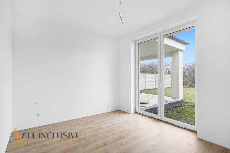 Pokoj v rodinném domě s velkým oknem a podlahou s dřevěným dekorem.