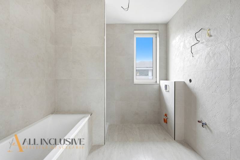 Koupelna v rodinném domě s vanou, oknem a světlými obklady.