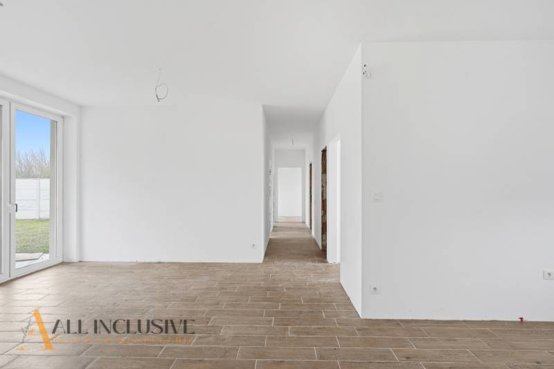 Bílá chodba v rodinném domě s podlahou s dřevěným dekorem a prosklenými dveřmi do dvora.