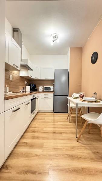 Kuchyně v 2-pokojovém bytě s bílými skříňkami a podlahou s dřevěným dekorem.