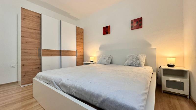 Ložnice v 2-pokojovém bytě s velkou postelí, šatní skříní a podlahou s dřevěným dekorem.