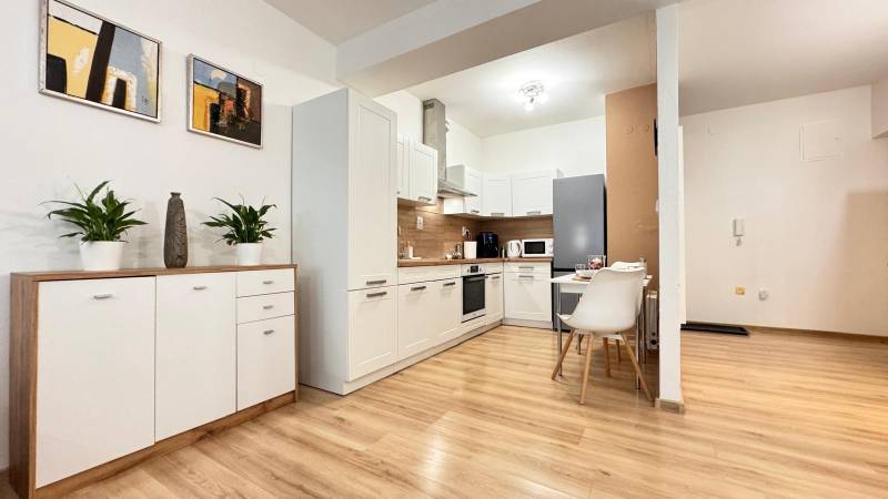 Kuchyně v 2pokojovém bytě s bílými skříňkami a podlahou s dřevěným dekorem.